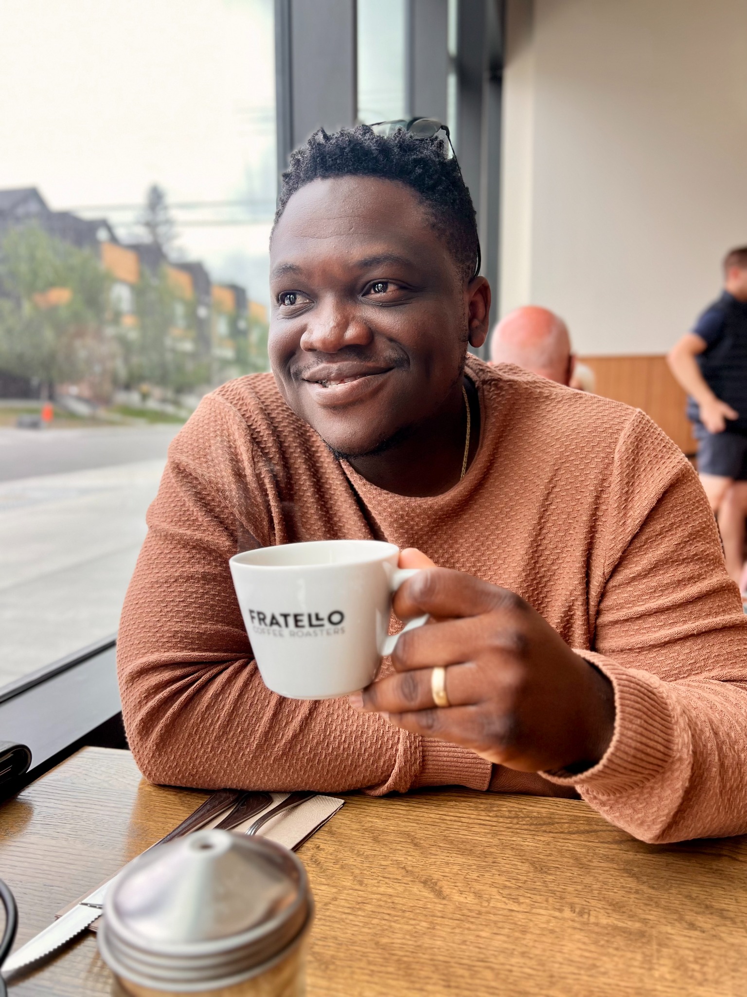 David Abolarin seated beside a café window, holding a coffee